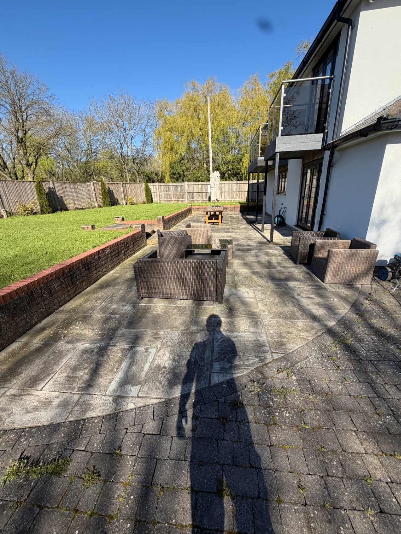 Large rear patio beside a raised lawn and balcony before cleaning